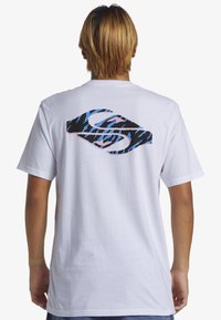 Camiseta de algodón blanca con un gran diseño gráfico en la parte de atrás en negro, azul y rosa. Mangas cortas y cuello redondo estándar.