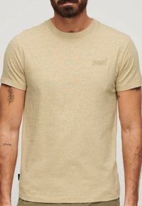 Beige short-sleeve t-shirt made from soft, textured fabric. Features a small, embroidered logo on the chest and a classic round neckline.