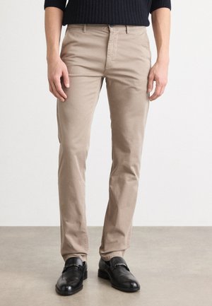 Beige katoenen chinos met slim fit, voorzien van zijzakken en een gladde textuur, gecombineerd met zwarte leren loafers.