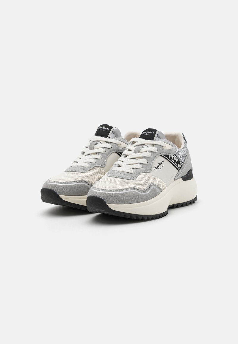 Zapatillas con una combinación de ante gris y malla, con una media suela blanca, detalles en negro y un talón texturizado. Los cordones son blancos; etiqueta del logo en la lengüeta.