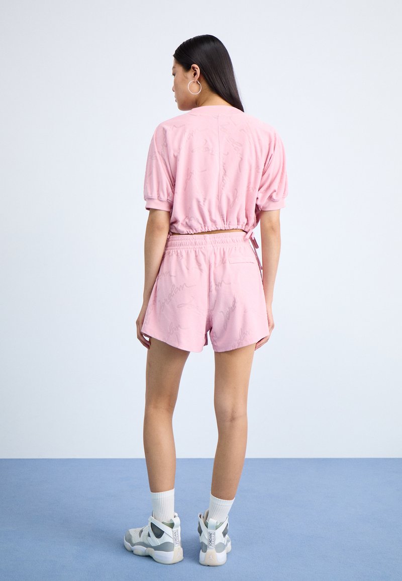 Completo corto composto da top rosa a maniche corte e pantaloni corti realizzati in un tessuto testurizzato con un motivo sottile. Abbinato a scarpe alte e calzini bianchi.