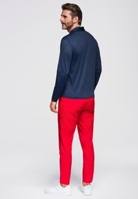 Polo a maniche lunghe di colore blu navy con colletto, abbinato a pantaloni aderenti di un vivace rosso. Sneakers bianche completano l'outfit. Tessuti con trame morbide.