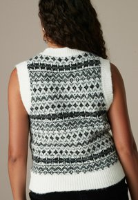 Pull sans manches en maille avec un motif flocon de neige en noir et blanc, col et ourlet côtelés, texture douce et coupe ajustée.