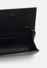 Czarny, teksturowany wnętrze torby z zapięciem na zatrzask, z akcentem w postaci łańcucha oraz kieszonką na kartę. Wykonana z materiału o gładkim wykończeniu.