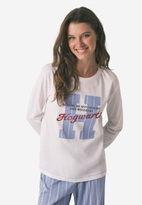 Maglietta bianca a maniche lunghe con una grafica a righe blu e testo rosso che dice "Hogwarts School of Witchcraft and Wizardry". Abbinata a pantaloni a righe blu.