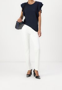 Top azul marino de manga corta con acentos con volantes, combinado con pantalones blancos de pierna recta y zapatos de tacón negro con punteras metálicas.