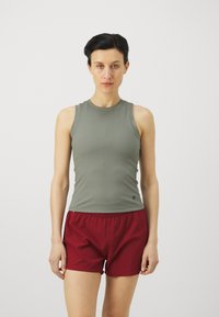 Khaki bezrukávový top s žebrovanou strukturou, spárovaný s červenými šortkami s elastickým pasem. Jednoduchý design, žádné nápadné vzory nebo akcenty.