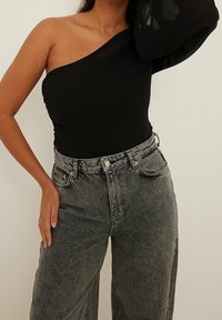 Svart bodysuit med en axel, kombinerad med högmidjade, löst sittande grå denimjeans. Jeansmodellen har en design med fem fickor och lätt slitage.