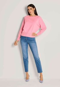Rosa Strickpullover mit langen Ärmeln und geripptem Saum, kombiniert mit eng anliegenden blauen Jeans und blauen High Heels mit floralen Akzenten.