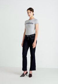 Grå tettsittende t-skjorte med teksten "COPENHAGEN", kombinert med mørk denim flared jeans og spisse svarte hæler, mot en nøytral bakgrunn.