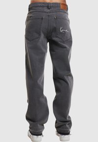 Vaqueros de corte relajado en gris oscuro con bolsillos traseros, logo bordado en blanco en el bolsillo derecho, dobladillos deshilachados, combinados con zapatillas blancas.