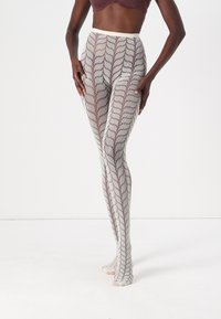 Sheer, patterned leggings in light beige with a zigzag design. High-waisted, form-fitting with a smooth texture and open toe accents.