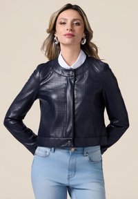 Giacca di pelle blu navy con design perforato, chiusura a scatto, colletto rotondo e maniche lunghe, abbinata a jeans blu chiaro.