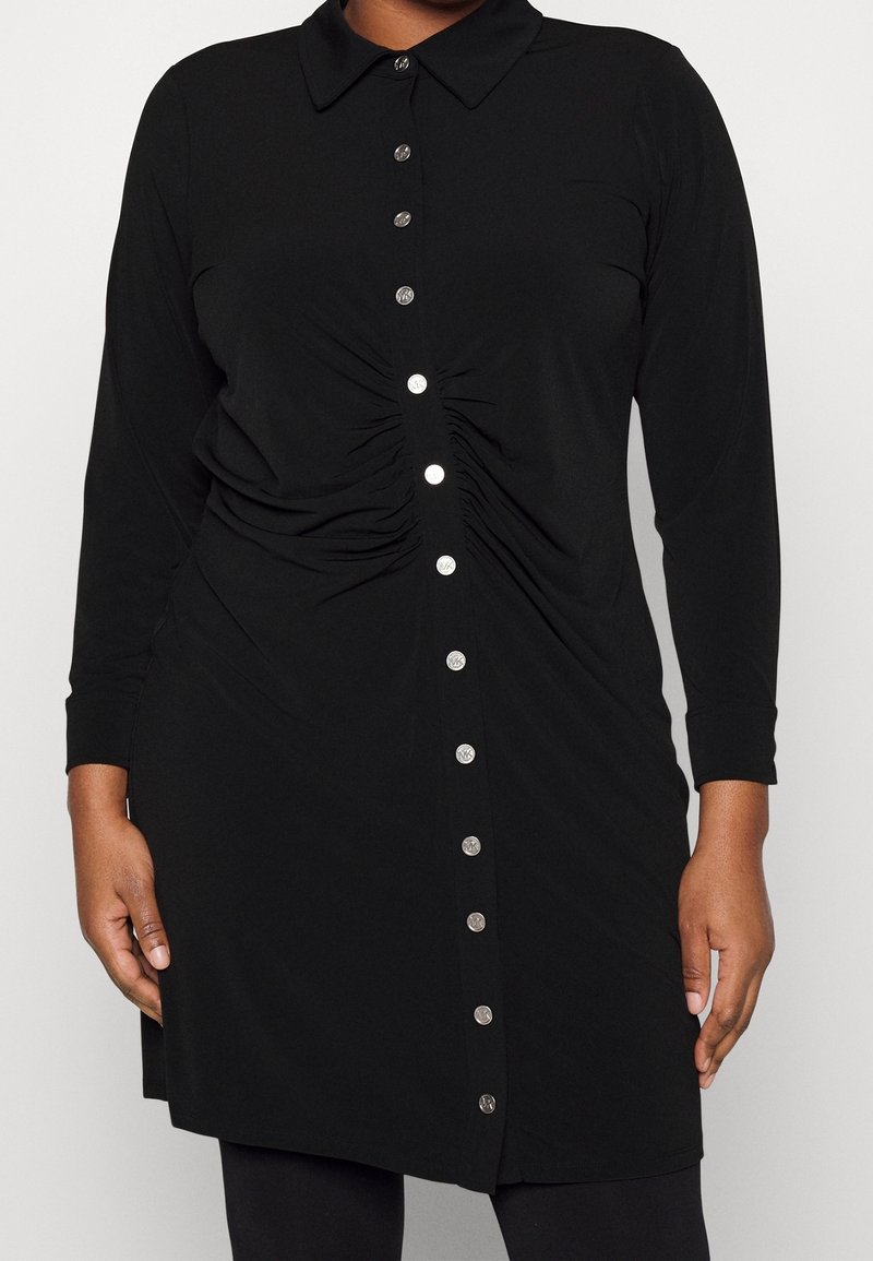 Vestito camicia nero realizzato in tessuto morbido, con colletto, maniche lunghe, chiusura centrale con bottoni argento e dettagli arricciati sui lati.