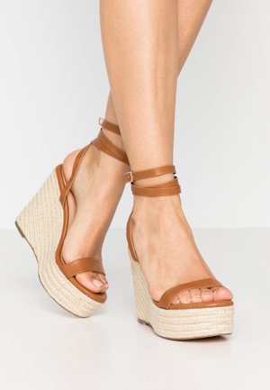 Brązowe skórzane sandały na koturnie z plecioną platformą z juty, z dwiema smukłymi paskami na stopie i paskiem na kostkę dla bezpiecznego dopasowania.