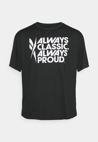 Černé tričko s krátkým rukávem má tučné bílé písmo: "VŽDY TRADIČNÍ. VŽDY HRDÝ." Text je zarovnán na střed s hladkým, matným povrchem.