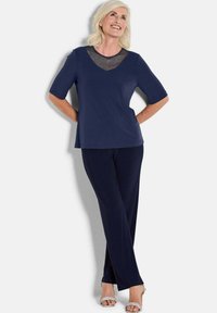 Marineblaues Outfit, bestehend aus einem kurzärmeligen Oberteil mit einem transparenten Netz-Ausschnitt und langen Hosen. Der Stoff wirkt weich mit einer glatten Textur.