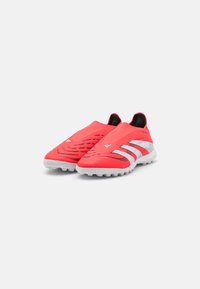 Red slip-on soccer shoes with a textured upper, featuring black accents and three white stripes on the side. Rubber cleated outsole.