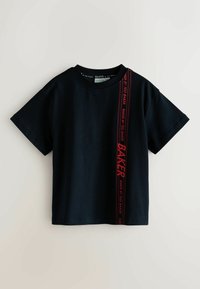 Mustast puuvillast lühikeste varrukatega T-särk, millel on tugeva punase vertikaalse logoriba ühe külje ääres ja ümmargune kaelus.