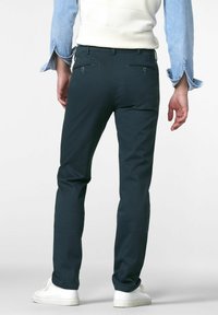 Donkergroene rechte broek met twee achterzakken, een rechte voorkant en een gladde textuur. Gekleed met witte sneakers en een spijkerblouse.