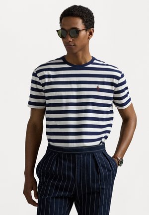 Marineblå og hvidstribet bomulds T-shirt med rund hals. Har et lille rødt logo på brystet og er parret med stribede bukser.