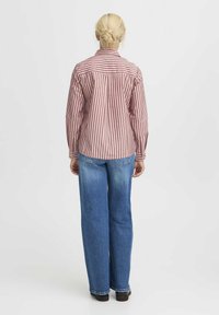 Camicia a righe rosse e bianche con un fit rilassato, abbinata a jeans a gamba larga blu e scarpe nere. Vista da dietro.