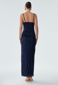 Navy sequin evening gown with slim straps, fitted bodice, and a straight floor-length skirt, showcasing a textured, glittering surface.