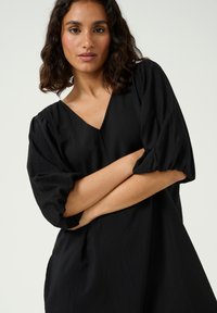 Black dress with a V-neck, puff sleeves, and a loose fit. Made from lightweight, textured fabric with subtle drape.