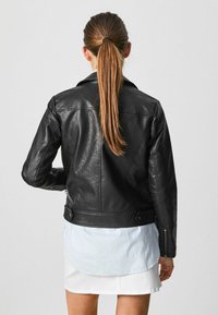 Giacca da motociclista in pelle nera con un design aderente, dotata di polsini con zip e colletto a punta. Presenta una texture liscia e cuciture strutturate.