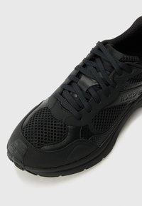 Zwarte sportieve schoen met een bovenwerk van mesh en synthetisch leer, voorzien van ronde veters, een gevoerd kraagje en een gestructureerde buitenzool voor grip.