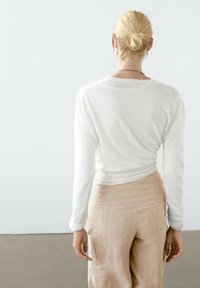 Witte top met lange mouwen, een ronde halslijn en een geribbelde zoom, gecombineerd met lichtbeige wijde broekspijpen met subtiele verticale strepen.