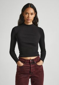 Fekete bordázott hosszú ujjú felső magas nyakkal, amelyhez bordó, magas derekú farmernadrág tartozik, elülső zsebekkel és gombos záródással.