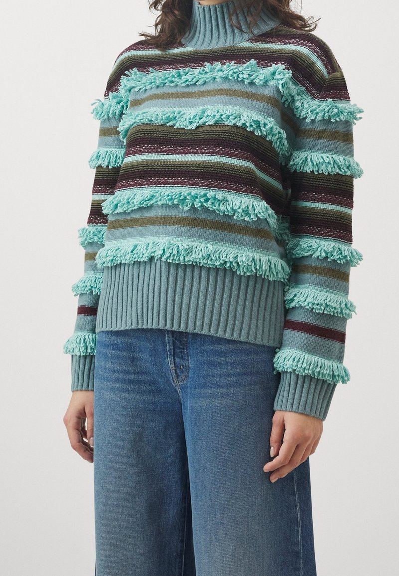 Raidallinen neulottu villapaita petroolin, ruskean ja burgundin sävyissä, jossa on teksturoidut hapsuaksentit. Resorit hihansuissa ja helmassa. Rentoa istuvuutta.