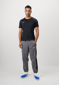 Black athletic t-shirt with short sleeves and a gray shoulder accent, paired with gray track pants featuring a black side panel and Nike logo.