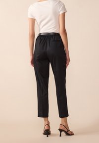 Czarne, dopasowane spodnie o luźnym kroju, z elastycznym paskiem w talii i bocznymi kieszeniami. Połączone z dopasowanym białym T-shirtem i czarnymi szpilkami.