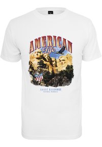 Valge puuvillane T-särk, millel on Mount Rushmore'i graafika. Julge punane "AMERIKA ELU" tekst kotka ja mälestuspiltide kohal.