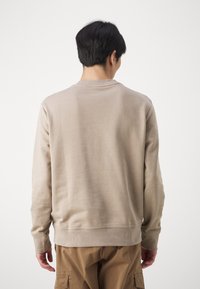 Sudadera de algodón beige con cuello redondo, puños y dobladillo acanalados. Tejido texturizado; la imagen muestra la parte posterior sin logotipos ni patrones visibles.