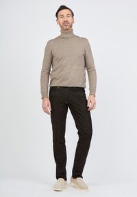 Beżowy sweter z golfem, dopasowany krój, miękka faktura. Czarne dżinsy, wąski krój, trwały materiał. Jasne buty wsuwane dopełniają stylizację.