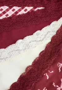 Textiel in tinten van kastanjebruin en roomkleur, met kantafwerkingen met bloemmotieven, en een roze geruit stof op de achtergrond.