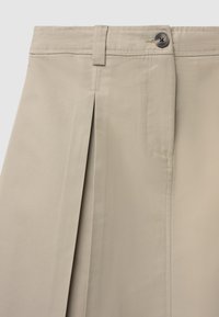 Jupe beige ajustée avec plis avant, fermeture à boutons, poche latérale, texture lisse et lignes épurées pour un look structuré.