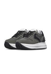 Sneakers grigi in suede con dettagli in pelle nera, particolare texturizzato sul tallone e lacci neri. Presentano un'intersuola bianca e una suola in gomma.