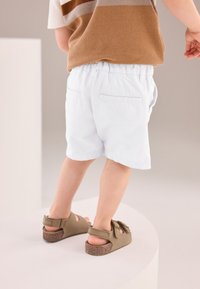 Pantalones cortos azul claro con cinturilla elástica, combinados con sandalias verde oliva que tienen un detalle de lazo y suelas de corcho. Diseño simple y funcional.