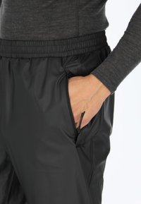 Zwarte sportbroek met een ritssluitingzak, elastische tailleband en een gladde, strakke textuur. Gecombineerd met een grijze lange mouw top.
