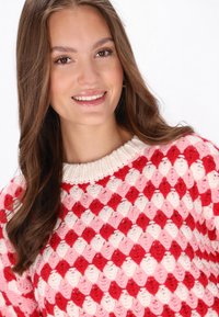 Red and pink patterned sweater featuring a textured diamond design, with a ribbed cream neckline and soft yarn material.