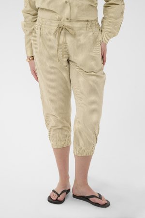 Beige and white striped cropped pants with drawstring waist worn with matching long-sleeve top and black flip-flops.