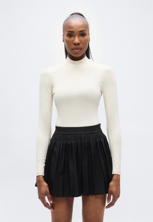 Hosszú ujjú, krémszínű felső magas nyakkal, fekete redős szoknyával, gumis derékpánttal. Sima szövet textúra.