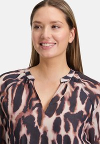 Leichte Bluse aus einem fließenden Stoff mit einem auffälligen Tierdruck in Braun- und Beigetönen, mit einem kleinen V-Ausschnitt und Raffungen an den Schultern.