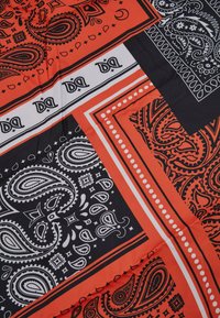 Bandana med røde, sorte og hvide paisley-mønstre. Glat stof med kontrasterende kanter og indviklede designs overalt.