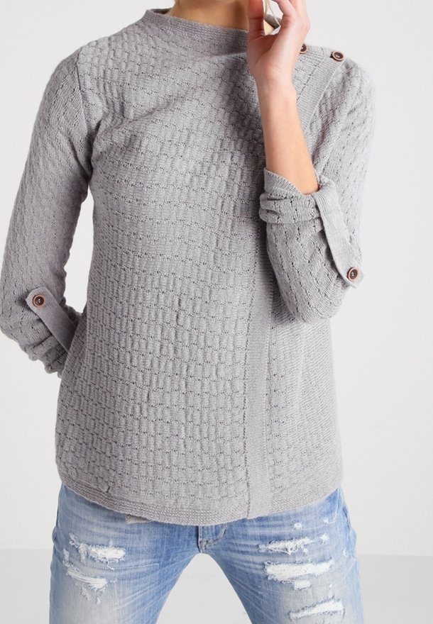 Sweater gris texturé avec un col haut et des accents de boutons sur les manches retroussées, associé à un jean bleu déchiré.