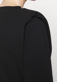 Schwarz langärmliges Oberteil mit einem runden Ausschnitt und subtilen Raffungselementen an der Schulter. Glattes Baumwollgewebe mit lockerer Passform.